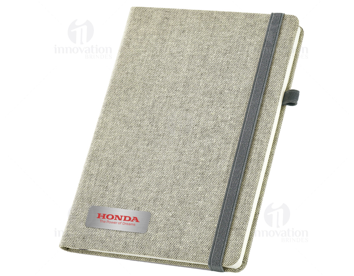 Caderno capa dura com porta esferográfica e folhas não pautadas cor marfim. Fornecido em embalagem de non-woven. Esferográfica não inclusa.