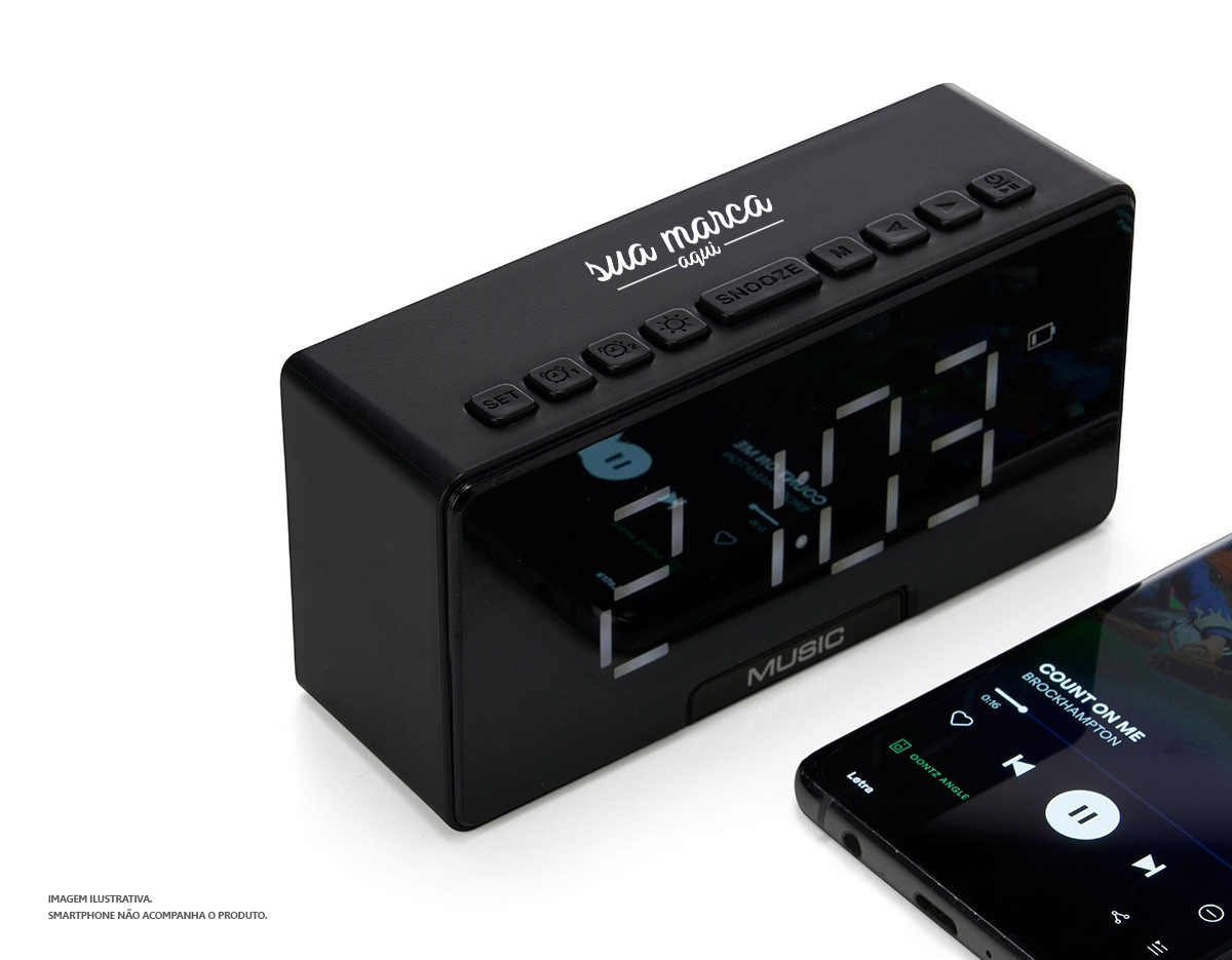 Caixa de som multimídia com relógio despertador e suporte para celular. Produzida em plástico e com borrachas antiderrapantes na área inferior, a caixa de som tem a área frontal com display de LED, além de um compartimento com suporte para celular – uma espécie de "gaveta" aonde é exibido (MUSIC), basta puxá-la ter acesso ao compartimento. A caixa de som executa nos modos bluetooth, rádio FM, cartão TF-microSD e entrada auxiliar P2. Acompanha cabo USB e manual em inglês.