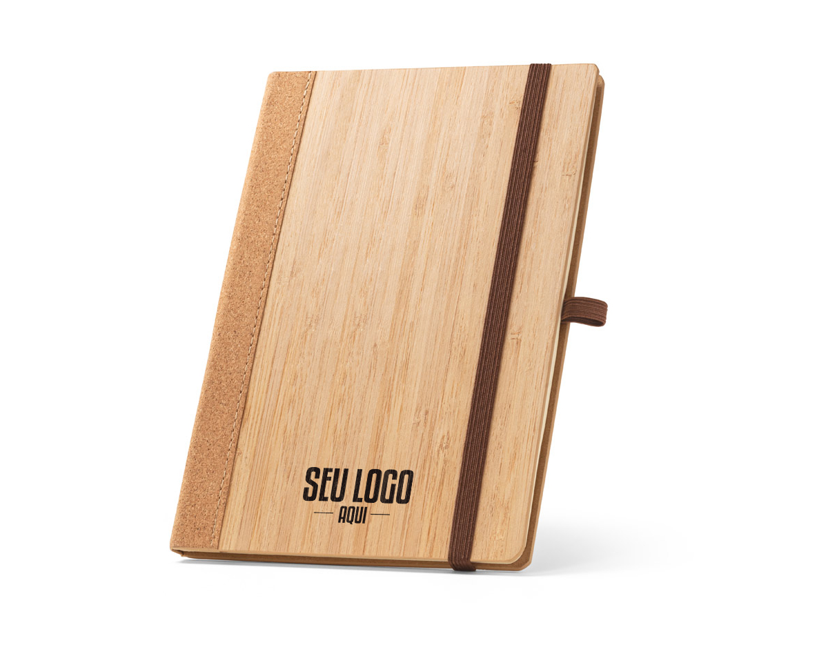 Caderno A5 de capa dura em folha de bambu e cortiça. Contém 80 folhas, em papel reciclado, pautadas cor de marfim, fita separadora, suporte para esferográfica (não inclusa) e elástico para fecho do caderno. A cor e o resultado da impressão nos materiais naturais pode variar entre produtos. 140 x 210 mm