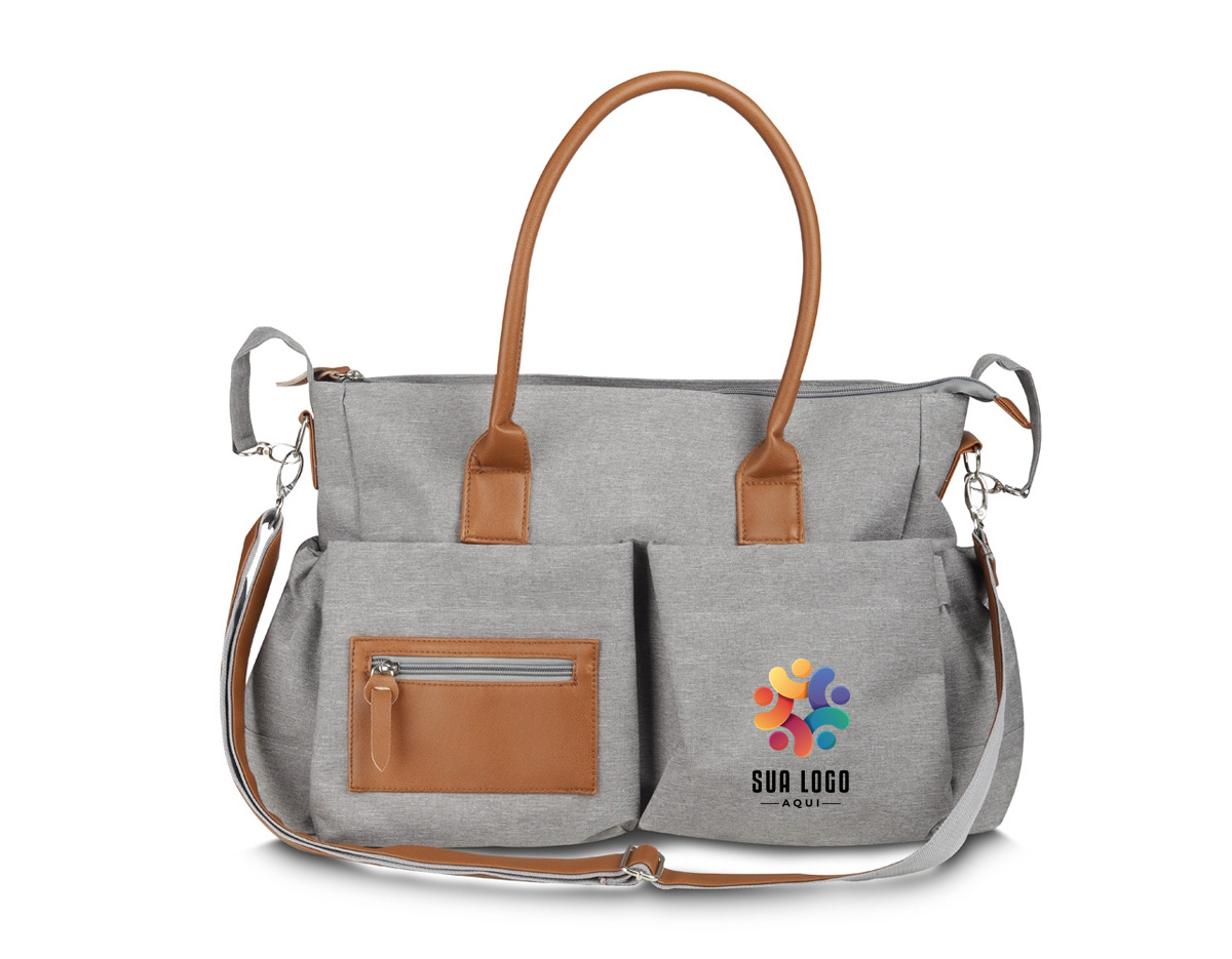 Nossa bolsa multifuncional de 17 litros foi pensada para atender diferentes necessidades do dia a dia. Feita em poliéster com tecido resistente à água, ela traz detalhes em couro sintético que dão um toque moderno e sofisticado. Por dentro, é totalmente forrada em nylon e tem um espaço amplo com quatro bolsos, facilitando a organização de tudo o que for necessário. O fechamento principal é por zíper, com um charmoso detalhe em couro sintético. Já na parte externa, são seis bolsos ao todo: um com fechamento em zíper e detalhe em couro sintético, dois nas laterais e outros três com botão de ímã, garantindo praticidade e segurança para pequenos objetos. Para maior conforto, as alças permitem o uso tanto no ombro quanto nas mãos. E para quem precisa de ainda mais versatilidade, a bolsa conta com uma alça extra produzida em poliéster e detalhe em couro sintético ajustável e removível, além de um suporte, perfeito para prender em carrinhos de bebê, supermercado ou onde desejar. Essa bolsa é uma excelente opção de brinde, unindo modernidade e praticidade.