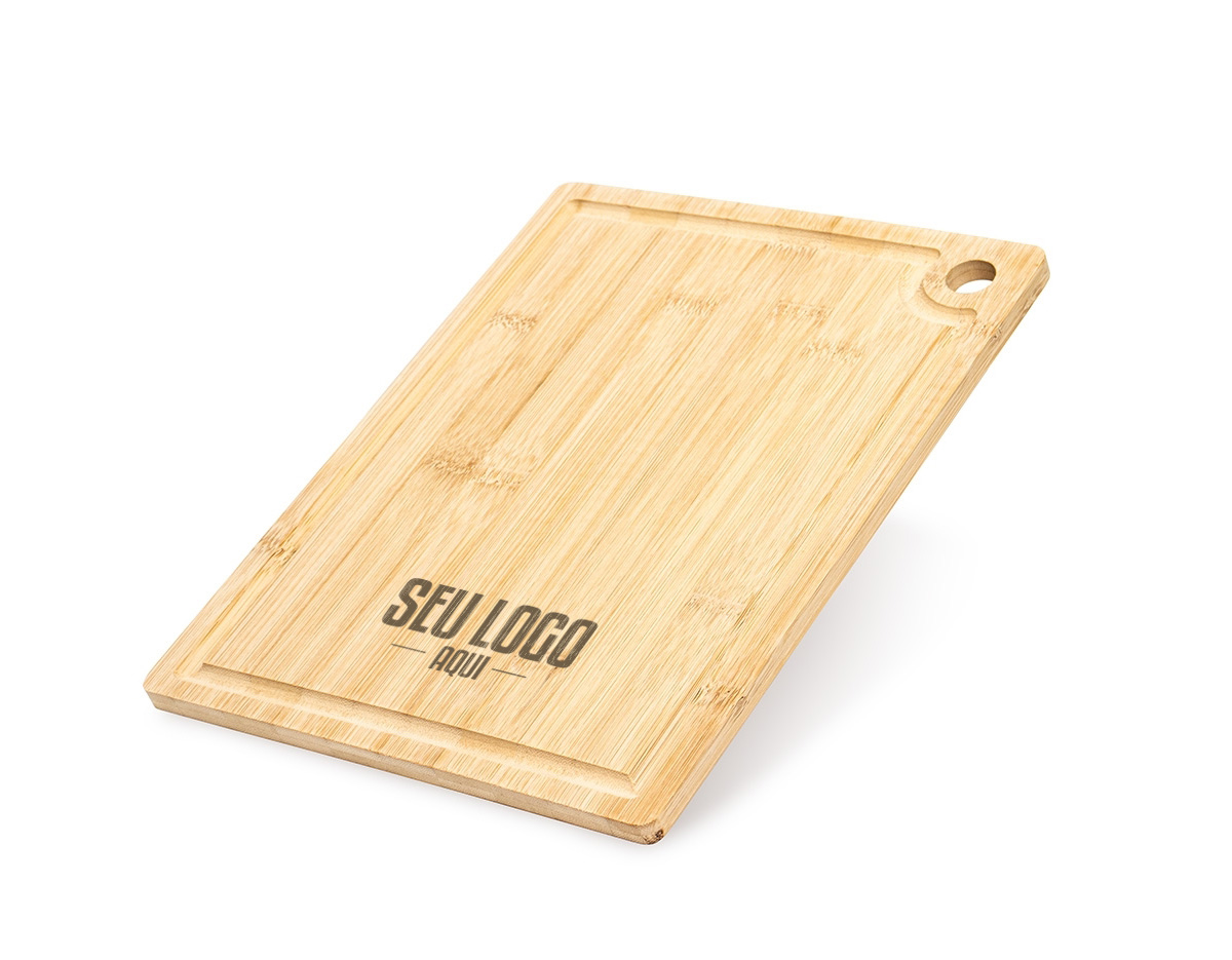 A tábua de corte é feita de bambu, um material resistente e sustentável. Ela possui uma canaleta ao redor para coletar líquidos e evitar sujeira. Além disso, conta com um acesso para gancho, facilitando o armazenamento e a organização na cozinha, tornando-a prática e funcional para o uso diário.