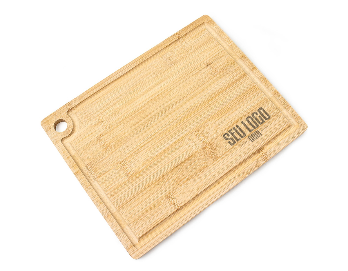A tábua de corte é feita de bambu, um material resistente e sustentável. Ela possui uma canaleta ao redor para coletar líquidos e evitar sujeira. Além disso, conta com um acesso para gancho, facilitando o armazenamento e a organização na cozinha, tornando-a prática e funcional para o uso diário.