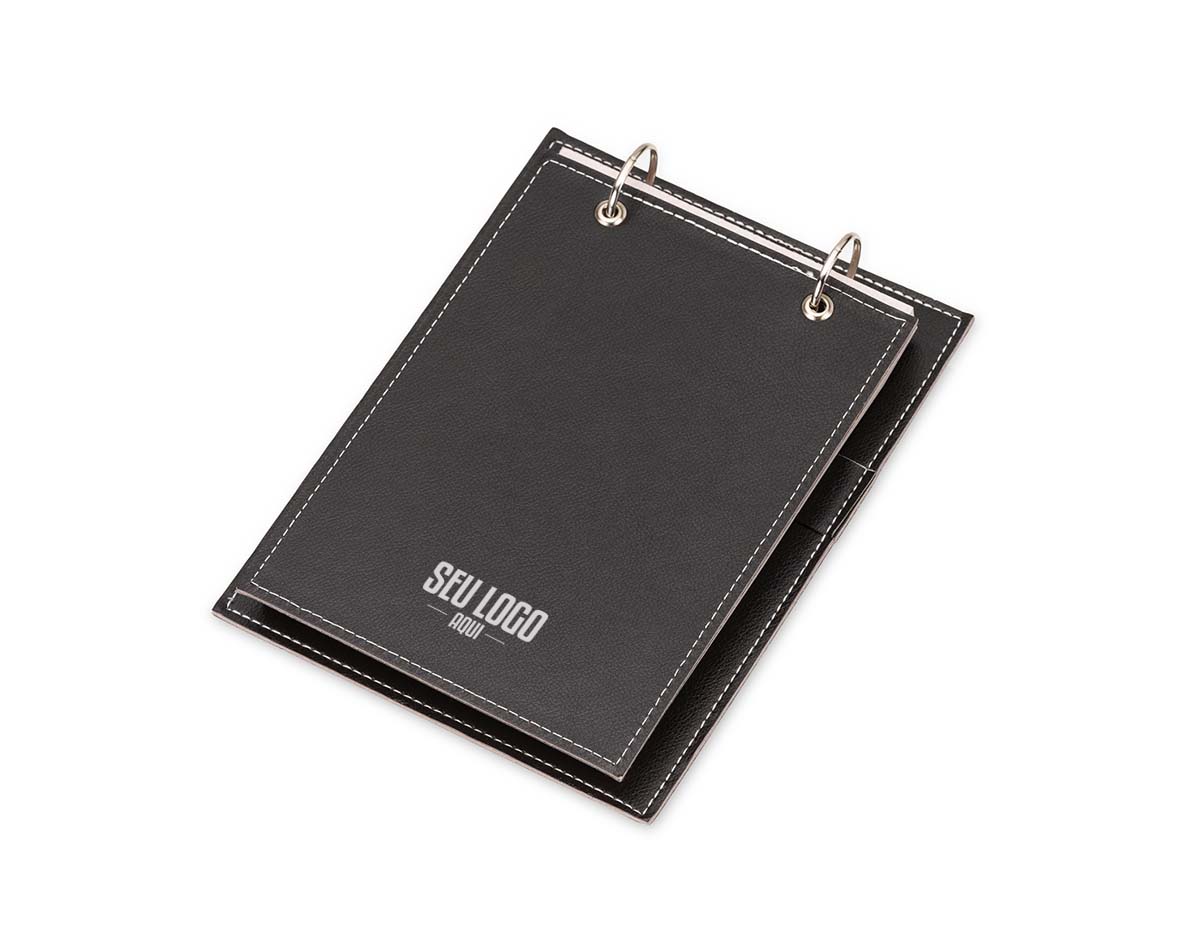 Bloco de anotações de mesa com trilho de ferro e capa em couro sintético. Contém suporte interno lateral para caneta (não inclusa) e cerca de 96 folhas recicladas com área destacável para facilitar o uso no dia a dia.