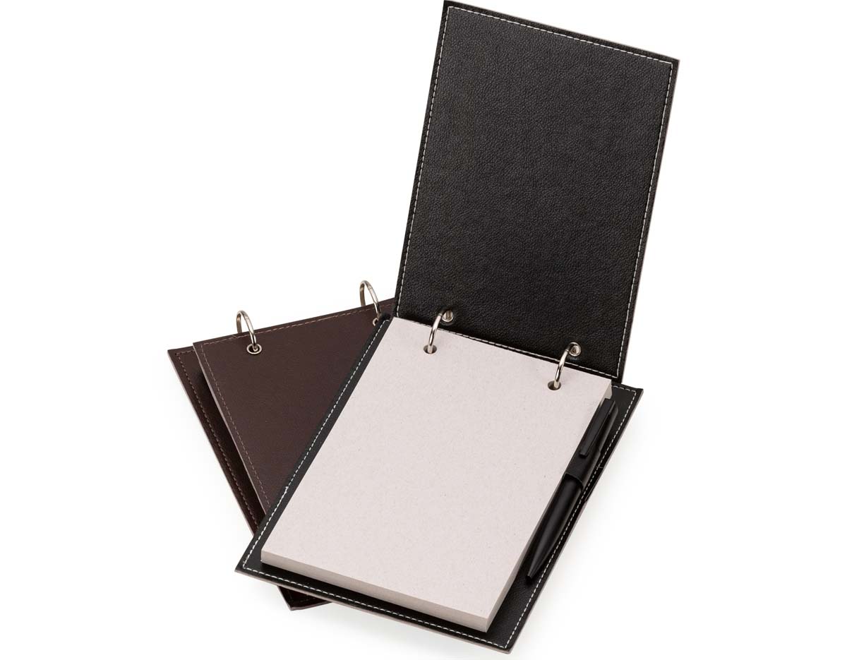 Bloco de anotações de mesa com trilho de ferro e capa em couro sintético. Contém suporte interno lateral para caneta (não inclusa) e cerca de 96 folhas recicladas com área destacável para facilitar o uso no dia a dia.