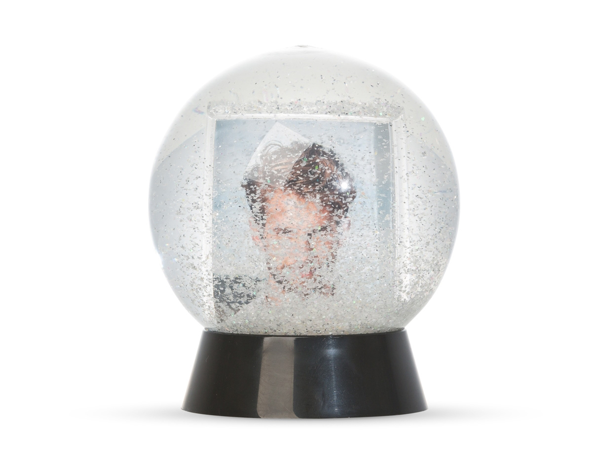 Globo de neve em plástico resistente, com glitter interno e porta-foto. A base preta é removível para inserção de uma foto no suporte interno, com dimensões de 8,5 cm x 4,7 cm, unindo decoração e funcionalidade em um só item.