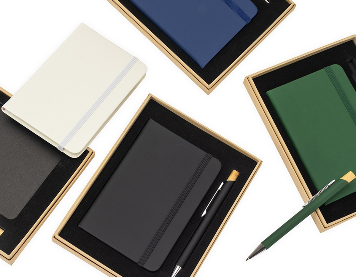 Kit executivo composto por uma caderneta e uma caneta. A caderneta possui capa dura, marca-páginas em fita de cetim e elástico para fechamento, além de aproximadamente 80 folhas com pauta. Por sua vez, a caneta metálica conta com detalhe em bambu, acionamento por clique e carga esferográfica azul de 1,0mm. Acompanha uma caixa de papelão com berço interno em espuma.